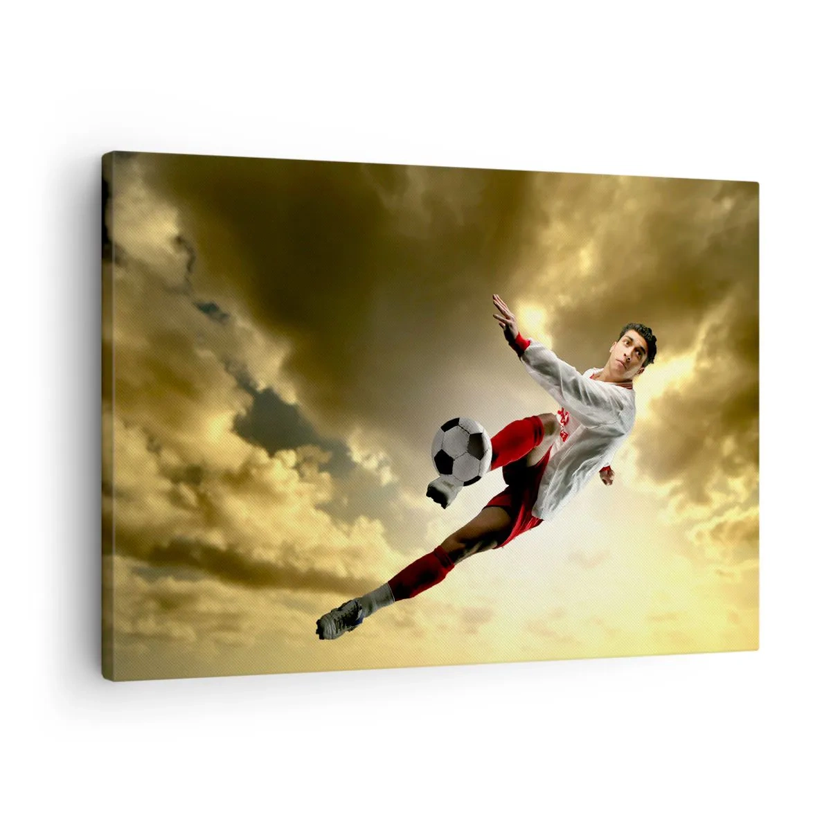 Vászonkép - Egy futballista dinamikus ugrásban rúgja a labdát az ég felé - 70x50cm - Futball Mennyország - Modern fali dekoráció nappalihoz és hálószobához ARTTOR