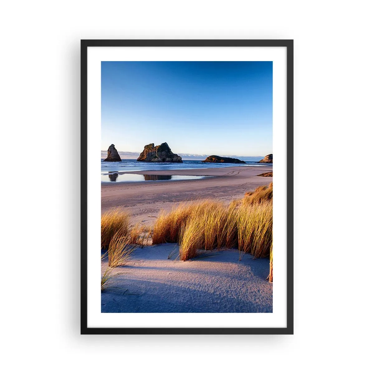 Poszter fehér keretben - Festői strand fűvel és sziklákkal, a hátterében a nyugodt óceán - 50x70cm - A nyugalmat keresőknek - Modern fali dekoráció nappalihoz és hálószobához ARTTOR